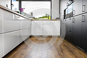 A modern kitchen with white and black fronts and a large corner window, vinyl panels on the floor.