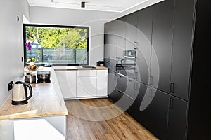 A modern kitchen with white and black fronts and a large corner window, vinyl panels on the floor.