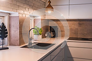 Modern kitchenette with white worktop, black sink and metal lamps