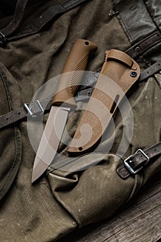 Modern knife with rubberized handle and plastic sheath. Cold steel lies on a vintage hiking backpack. Wooden back