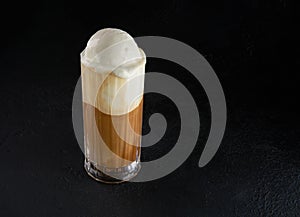 A modern, lactose free coffee drink or cocktail with ice cream and almond milk. Macchiato in a tall glass on a dark