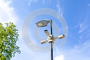 Modern lamppost and 3 surveillance cameras mounted in different directions in public park. Public space security systems