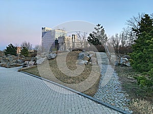 A modern landscaped park with benches and sidewalks. Skyscrapers and modern buildings.