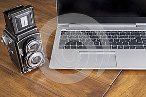 Modern laptop computer next to an old twin lens camera, contrasting between modern and retro style