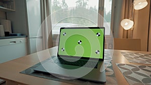 Modern laptop with green screen on wooden kitchen table