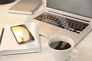 Modern laptop, smartphone, cup of coffee and notebook on white table, closeup