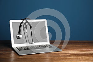 Modern laptop with stethoscope on table against color wall.