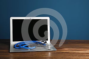 Modern laptop with stethoscope on table against color wall.