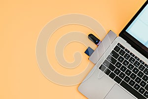 Modern laptop with USB Type-C adapter and flash drives is isolated on an orange background