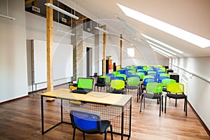 Modern lecture room with with colored chairs and interesting design, laptop on the table, green screen.