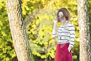 Modern Lifestyle and fashion Concepts: Positive and Smiling Caucasian Brunette Female with Sunglasses Posing in Fall Forest Outdo