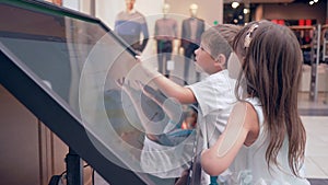 Modern little boy with girl uses Touchscreen of self-service machine For search information about location of halls and