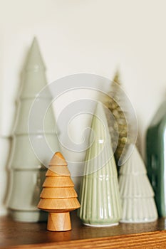 Modern little christmas trees on wooden shelf, stylish festive decor. Christmas miniature forest, wooden and ceramic trees. Merry