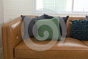 Modern living room with big comfortable leather sofa with green and black pillows.