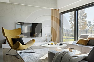Modern living room interior design with corner beige sofa, creative rounded coffee tables, mustard armchair and personal.