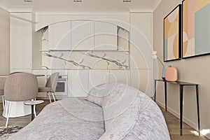 Modern living room interior in pastel colours with round dining table, beige chairs, creamy white furniture.