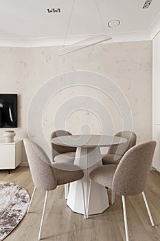 Modern living room interior in pastel colours with round dining table, beige chairs, creamy white kitchen furniture.