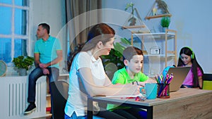 In a modern living room mother doing the home work with her little boy using laptop dad while other family members