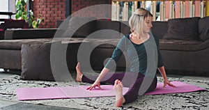 In a modern loft attractive blonde lady with a comfortable sportswear practicing yoga exercises for stretching the body