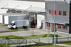 Moderní logistické centrum, bílá dodávka a přívěsy stojící na rampě