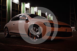 Modern luxury white sedan 2-doors sport car is parked at the night parking at the city neat the shopping center.