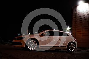 Modern luxury white sedan 2-doors sport car is parked at the night parking at the city neat the shopping center.