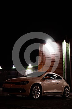 Modern luxury white sedan 2-doors sport car is parked at the night parking at the city neat the shopping center.