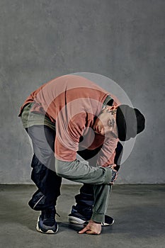 Modern male with tattooed face, beard. Dressed in colorful jumper, black pants and sneakers. Dancing on gray background