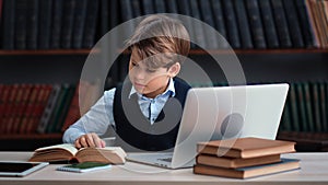 Modern male teen pupil doing homework at public library use laptop pc paper textbook e learning