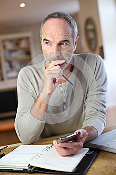 Modern man sitting at home working with smartphone and laptop