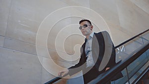 Modern man in stylish suit and sunglasses going down on escalator