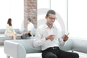 Modern man uses a digital tablet sitting in the office lobby.