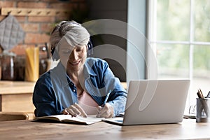 Modern mature 60s woman in headphones study on laptop