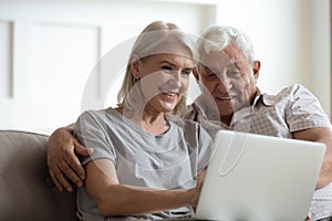 Modern mature couple using laptop relaxing at home