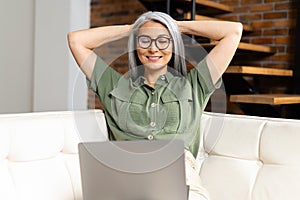 Modern mature 60s female enjoy leisure weekend at home, watching movie on computer gadget. Happy elderly woman sit relax