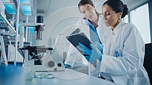 Modern Medical Research Laboratory: Two Female Scientists Working, Using Digital Tablet, Analysing