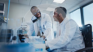 Modern Medical Research Laboratory: Two Smiling Male Scientists Working Together Using Microscope,