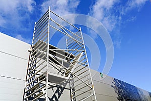 Modern metal scaffolding next to a new building gray sandwich panel wall, blue sky background