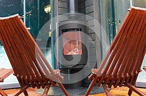 modern metal stove with burning wood and garden chairs around, no people