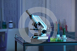 Modern microscope and glassware with colorful liquids on metal table in laboratory