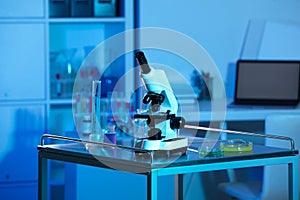 Modern microscope and glassware with colorful liquids on metal table in laboratory, toned in blue