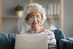 Modern middle-aged 60s woman using laptop relaxing at home