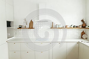 Modern minimal kitchen design. Stylish white kitchen cabinets with brass knobs, granite island, appliances and utensils on wooden
