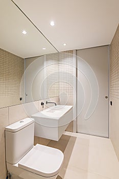 Modern minimalist bathroom interior design with white sink, toilet, beige tiles, and large mirror.