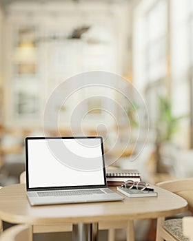 A modern, minimalist coffee shop features a white screen laptop computer mockup on a wooden table