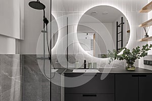 Modern minimalistic bathroom interior design with grey stone tiles, black furniture, eucalyptus in glass vase