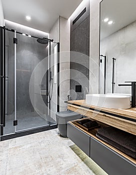 Modern minimalistic bright bathroom with wooden furniture, gray and beige stone tiles