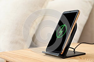 Modern mobile phone charging on wireless pad in bedroom, closeup. Space for text