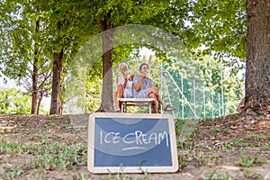 Modern mom and young daughter eating ice cream sitting on a deckchair in a water park on summer