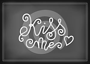 Modern mono line calligraphy lettering of Kiss me in white decorated with heart on chalkboard